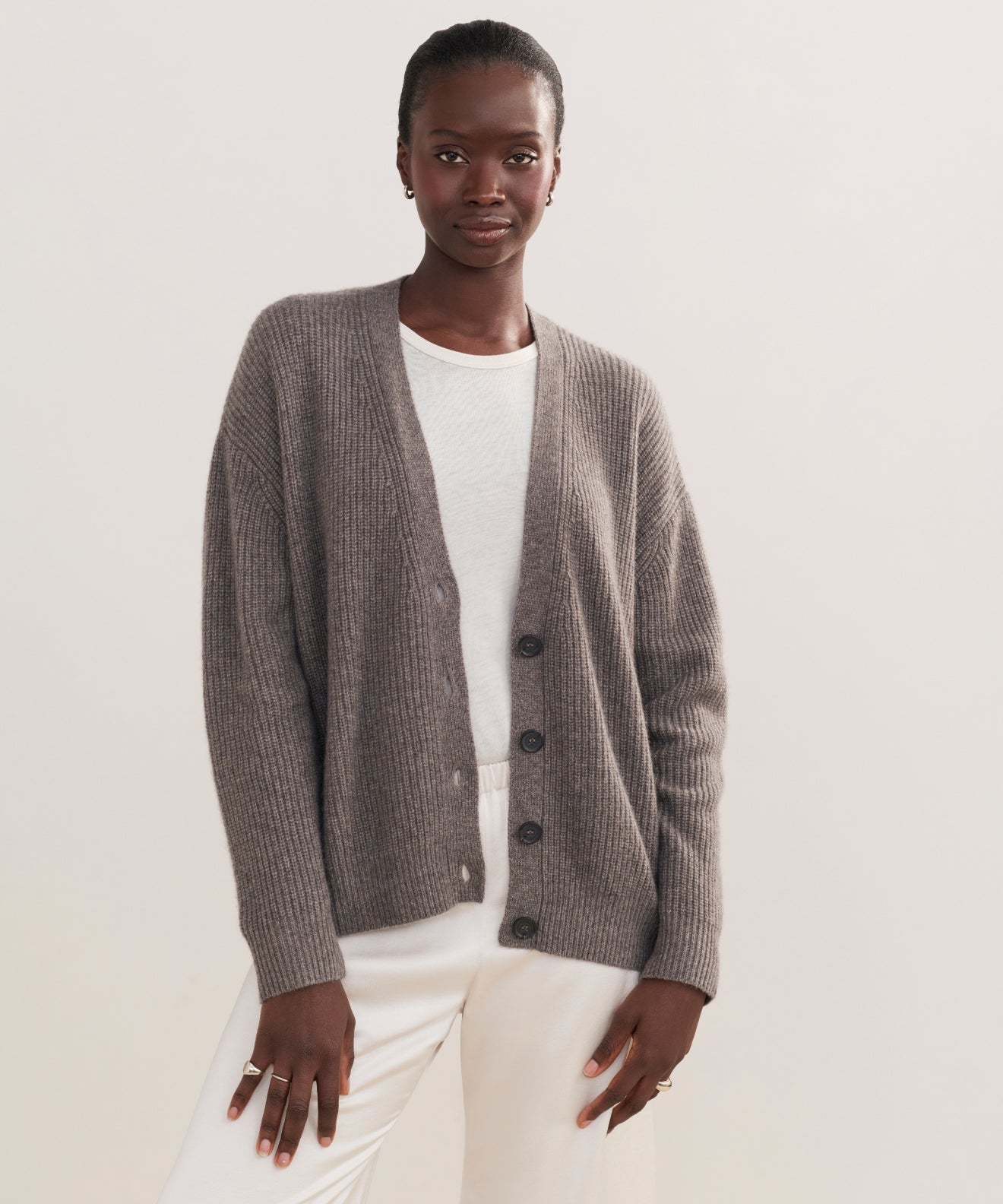 A person models the Cropped Cashmere Cocoon Cardigan in gray over a white shirt and pants, standing confidently against a plain light background.