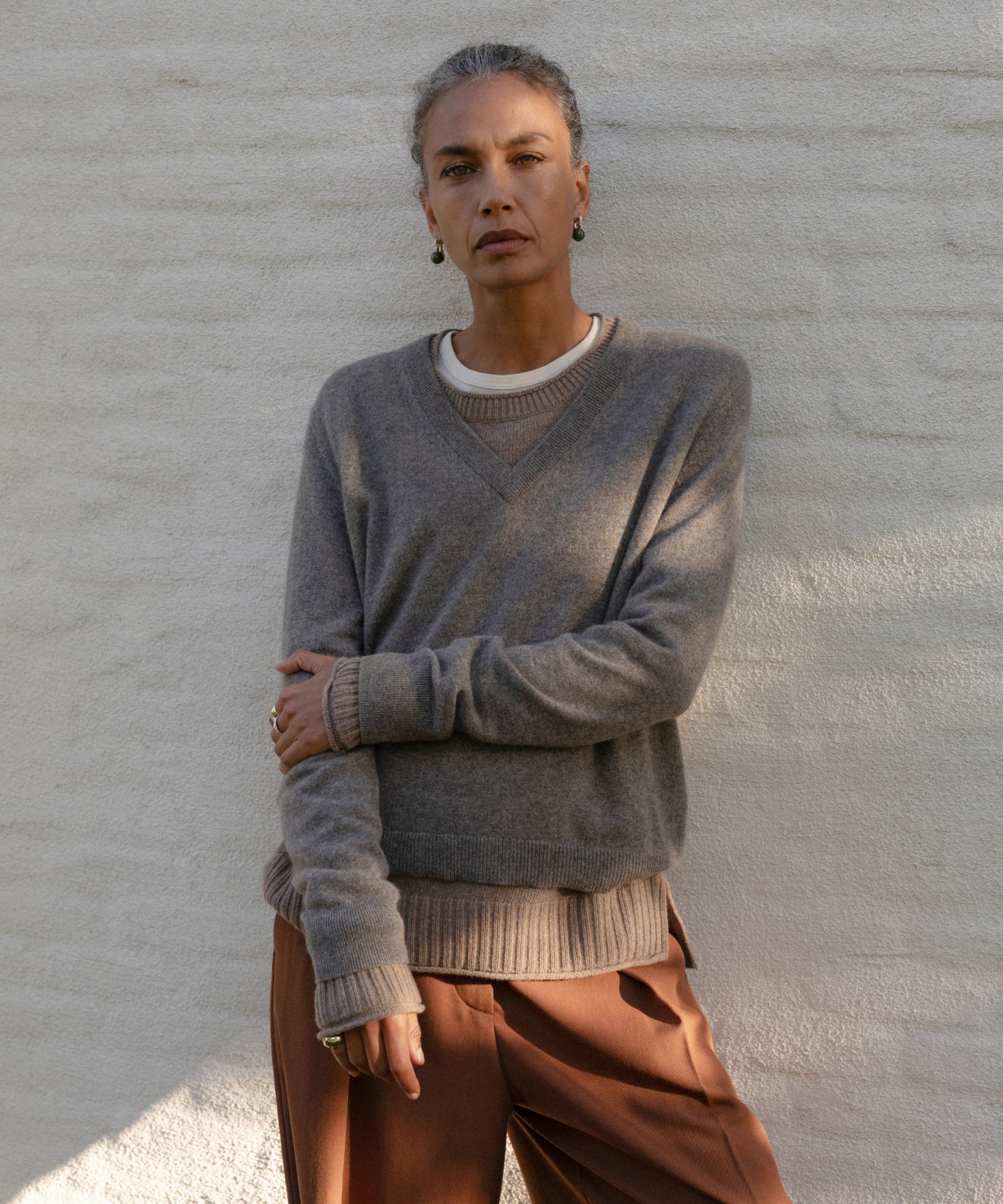 Model wearing a gray Flynn Cashmere Sweater and brown trousers against a light gray wall